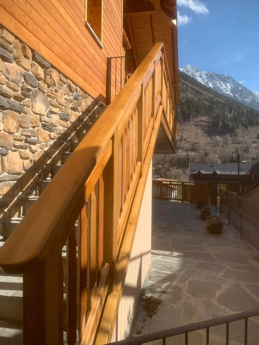 Scala esterna con ringhiera in legno chiaro e vista sulle montagne